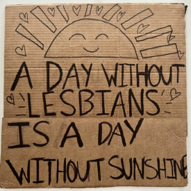 Cardboard sign brought to 2022 pride parade, this side "A Day Without Lesbians is a Day Without Sunshine" recreated from the San Francisco Gay Freedom Parade 1979 in black sharpie.