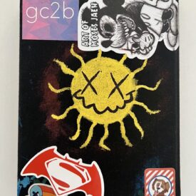 Black colored journal back with gc2b sticker, Mickey Mouse with "Art of Moses Jaen, drawing of a sun with X shaped eyes, Superman symbol inside Batman wings, a heart with trailing colors, and a cartoon dog surrounded by red and white stripes.
